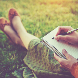 female hands with pen writing on notebook on grass outside